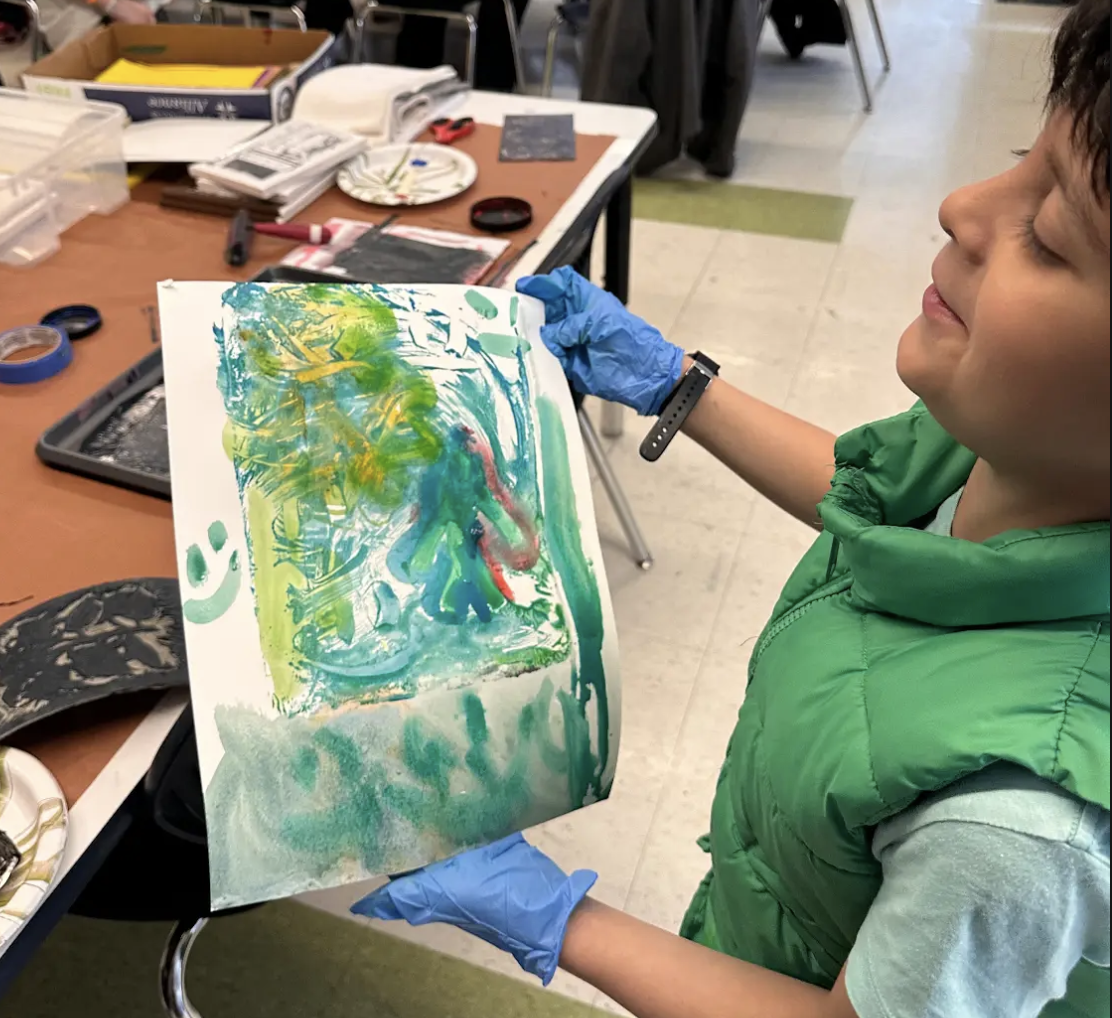 Student proudly displaying their artwork and smiling