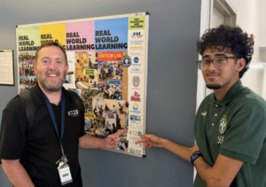 Student standing next to bulletin board with teacher